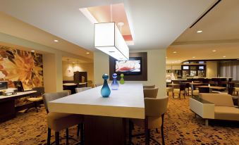 a modern lounge area with a long white table , chairs , and various seating options , including a bar and dining tables at Courtyard Newburgh Stewart Airport