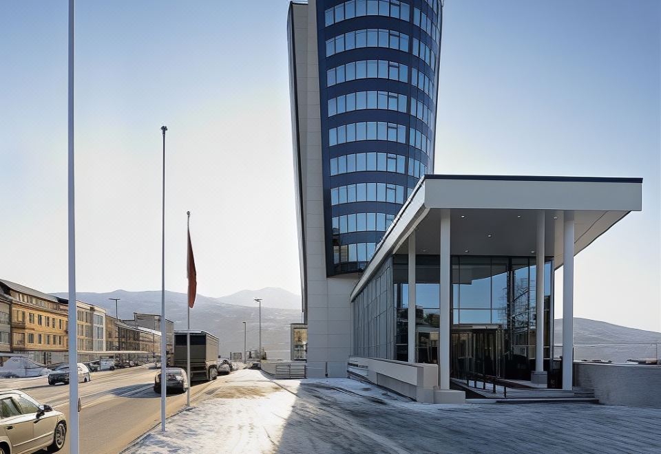 a modern building with a curved exterior and a flagpole in front of it , surrounded by snow at Scandic Narvik