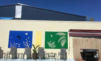 a patio area with a blue chair , a green chair , and a colorful mural on the wall at Black Marlin Motel