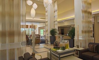 a modern hotel lobby with various seating arrangements , including couches , chairs , and potted plants , as well as a dining table at Hilton Garden Inn Jackson/Madison