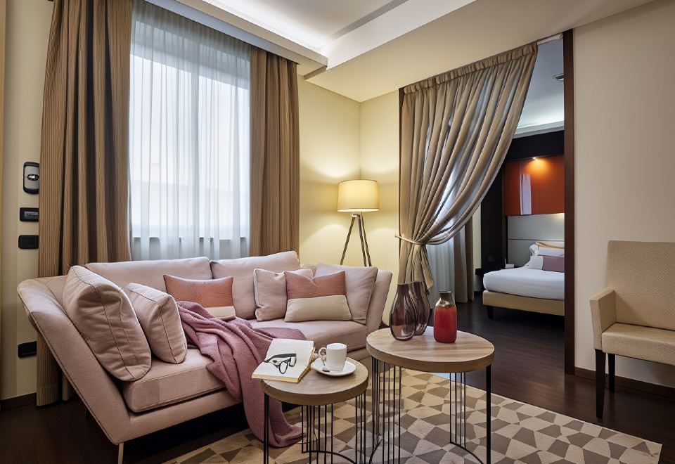 a modern living room with a pink couch , coffee table , and lamps , as well as a bedroom visible through a glass door at Winter Garden Hotel Bergamo Airport