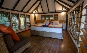 a cozy bedroom with a large bed , wooden floors , and a flat - screen tv mounted on the wall at Likuri Island Resort Fiji