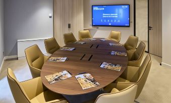 a conference room with a round table surrounded by chairs and a television mounted on the wall at Mercure Chartres Cathedrale