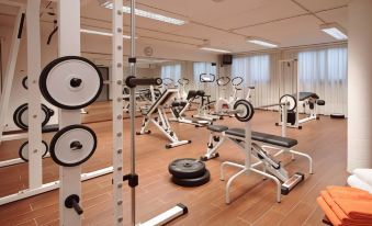 a well - equipped gym with various exercise equipment , including weightlifting machines and cardio machines , under bright lights at B&B Hotel Bologna