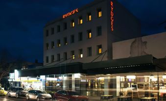 "a modern building with the name "" rydges "" lit up at night , surrounded by other buildings and cars on a street" at Saint Kilda Beach Hotel, an EVT hotel - Formerly Rydges St Kilda