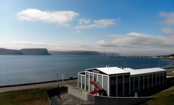 a large building with a red flag on top is situated near the water , overlooking a mountain at Fosshotel Westfjords