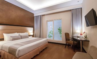 a large bed with white linens is in a room with wooden floors and a desk at Solaris Hotel Malang