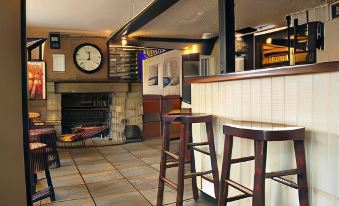 a bar with wooden stools and a clock on the wall , next to a fireplace at The White Hart