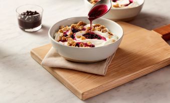 a white bowl filled with granola , topped with yogurt , and drizzled with dark syrup , placed on a wooden table at SpringHill Suites Madera