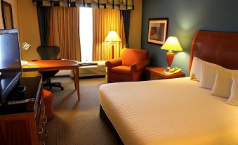 a hotel room with a bed , chairs , and desk , along with a window and lamp at Hilton Garden Inn Albany