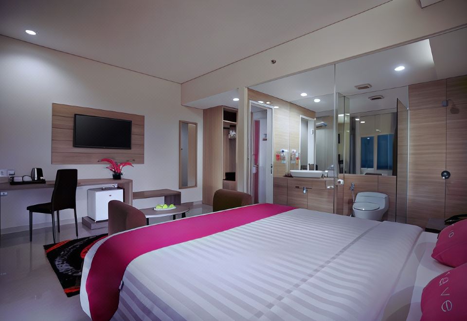 a modern hotel room with a large bed , pink bedding , and a bathroom visible through an open door at favehotel Langko Mataram - Lombok
