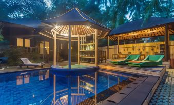 a luxurious poolside area with a gazebo , umbrellas , and sun loungers , surrounded by lush greenery and blue water at Coconut Boutique Resort