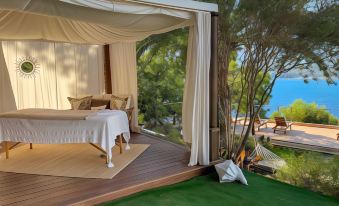 a bedroom with a bed and white sheets is shown with a view of the ocean at A’mare Corsica Seaside Small Resort