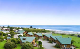 a group of wooden cabins situated near the ocean , with a car parked in the middle of the lot at Shining Star Beachfront Accommodation