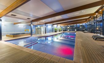 an indoor swimming pool with a blue tiled floor and wooden beams , surrounded by chairs and tables at Novotel Canberra