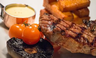 a steak on a plate , accompanied by a variety of vegetables and sauces , creating a delicious meal at The Mill Hotel