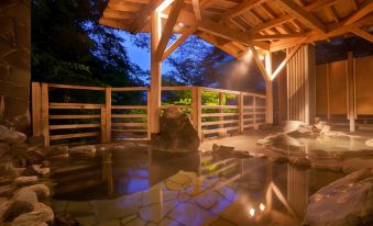 a wooden gazebo with a stone water feature in the middle , surrounded by trees and lit up at night at Zazan Minakami