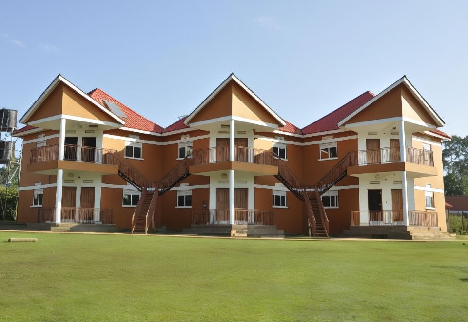 a large orange building with two balconies , surrounded by green grass and trees , under a clear blue sky at Country Inn Masindi