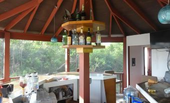 a bar with various bottles and glasses on the counter , under a wooden roof with trees in the background at Country Cove