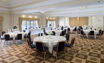 a large conference room with multiple round tables , chairs , and other furniture arranged for a meeting or event at Airport Inn Manchester