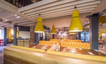 a modern restaurant with wooden tables , yellow chairs , and pendant lights , as well as a bar area at Crewe West