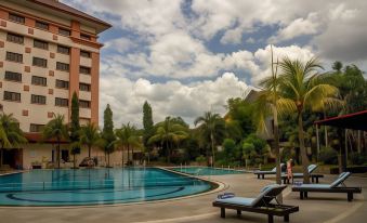 a large outdoor pool surrounded by palm trees and a building , with lounge chairs placed around it at The Sunan Hotel Solo