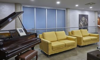 a living room with two yellow couches and a grand piano in the center , surrounded by windows at Hotel Concorde