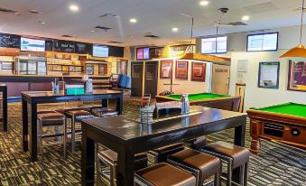 a room with a bar and pool table , surrounded by chairs and tables , has several televisions mounted on the wall at Everton Park Hotel