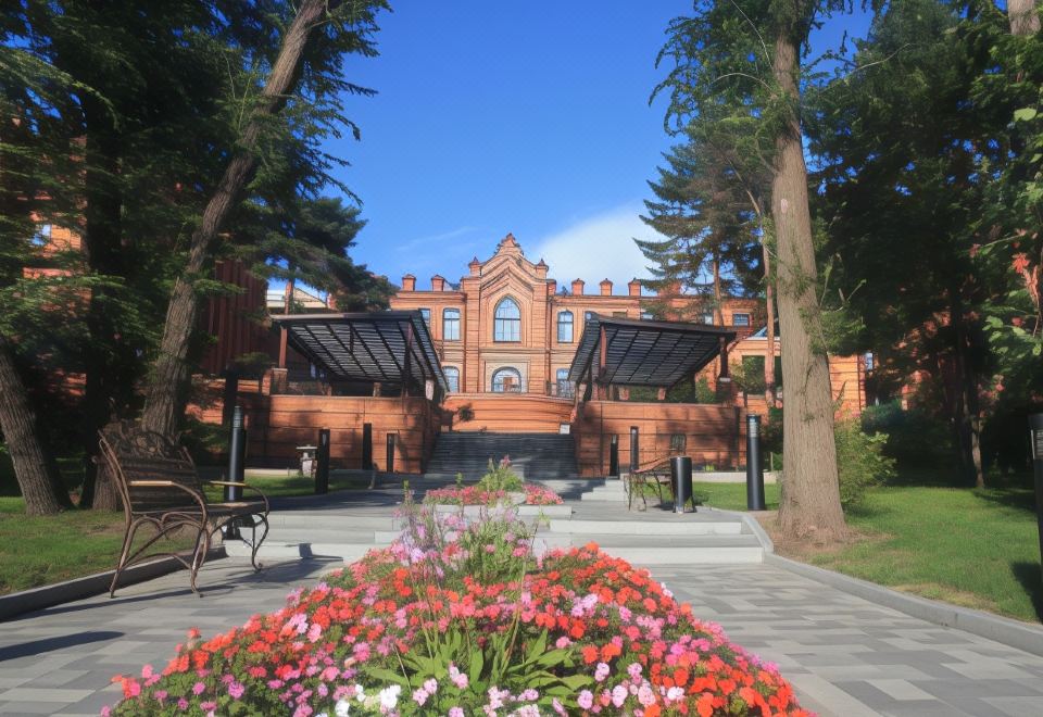 a red brick building surrounded by trees and flowers , with a paved walkway leading up to it at Parus