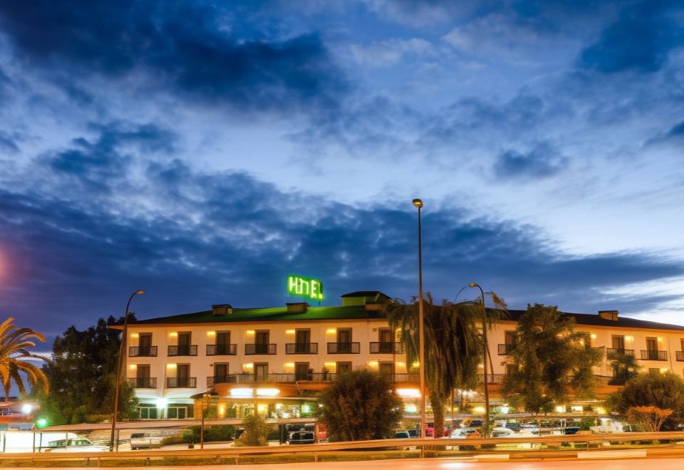 "a hotel building with the word "" hotel "" lit up at night , surrounded by other buildings and trees" at Zodiaco