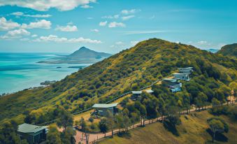 aerial view of a grassy hill overlooking a body of water , with several buildings on the hillside at Chalets Chamarel