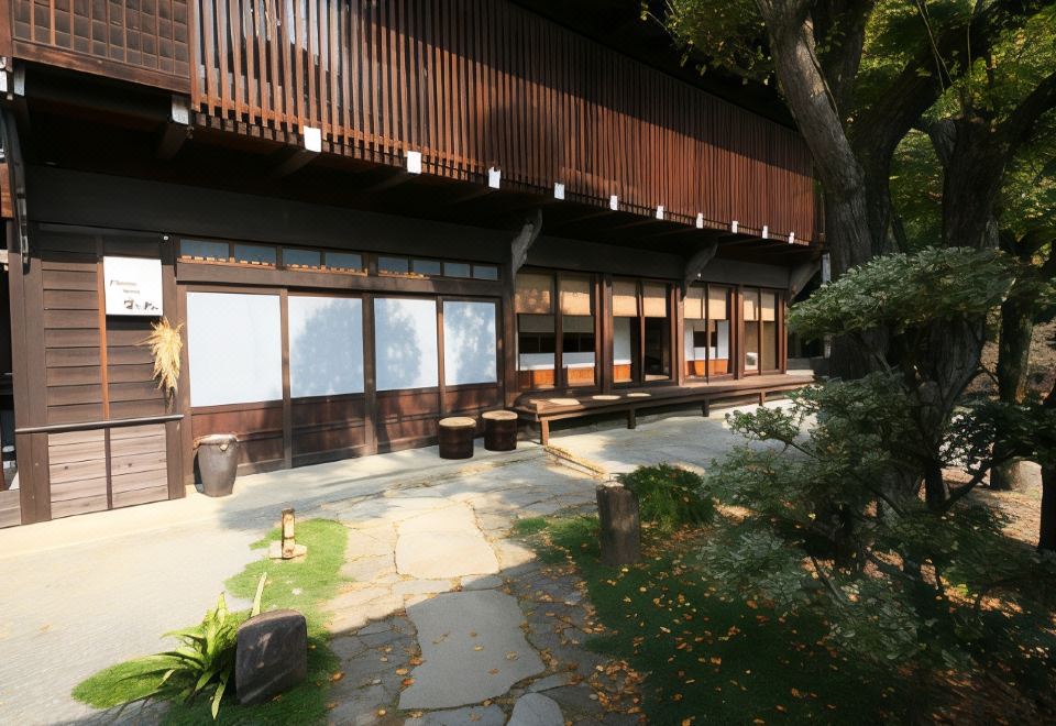 a modern building with wooden exterior , large windows , and stone steps , surrounded by trees and greenery at Fuefukigawa Onsen Zabou