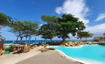 a large pool surrounded by lounge chairs and umbrellas , with a tree in the background at Bluewater Sumilon Island Resort