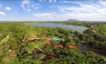 an aerial view of a forested area with a large body of water and buildings , including a red - roofed building at Habarana Village by Cinnamon