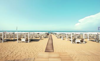 a wooden walkway leading to a sandy beach , with rows of lounge chairs and umbrellas set up along the way at Toscana Charme Resort