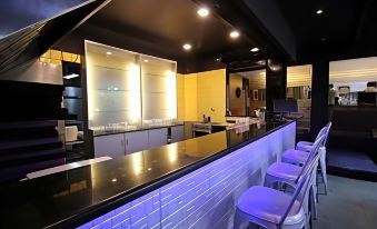 a modern bar with a black countertop and white stools , surrounded by yellow walls and glass doors at Hotel Woodland