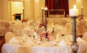 a large , well - lit banquet hall with multiple tables set for a formal event , including wine glasses , flowers , and napkins at Parklands Resort Mudgee