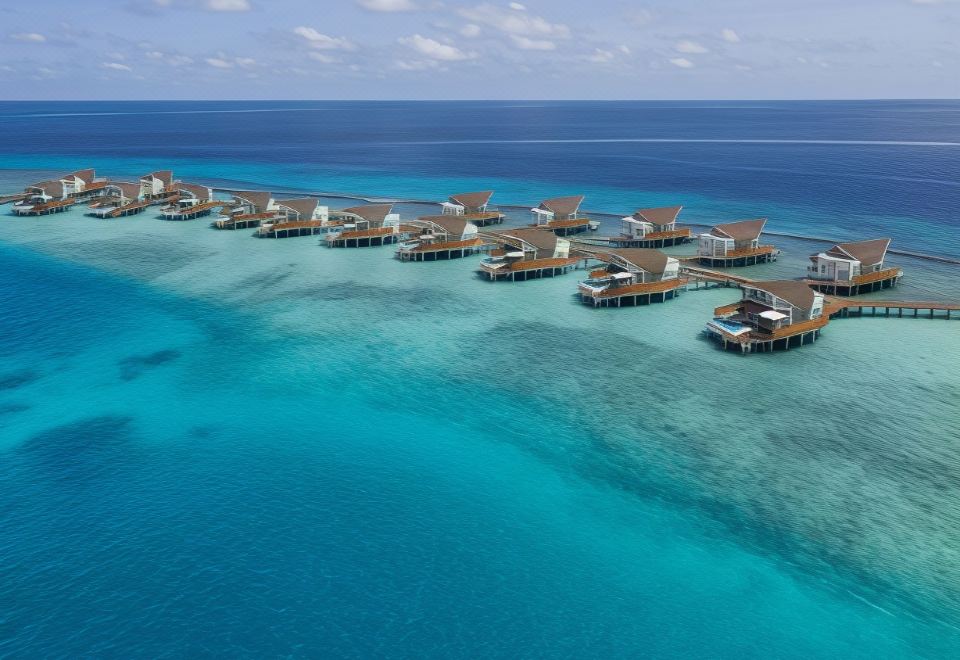 a tropical island with wooden bungalows , surrounded by clear blue water and clear skies at JW Marriott Maldives Resort & Spa