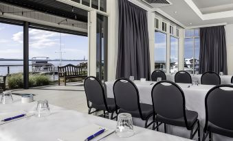 a large conference room with white tables and chairs , black chairs , and a view of the water at Anchorage Port Stephens