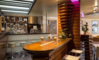 a modern bar with a wooden counter , two glasses of beer on the counter , and stools at Hotel Firenze