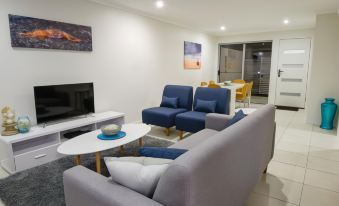 a modern living room with a gray couch , blue chairs , and a television on the wall at Direct Collective - Breeze on Brightwater