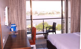 a bedroom with a bed , desk , and chairs , as well as a view of the water through a large window at Hotel Apaar