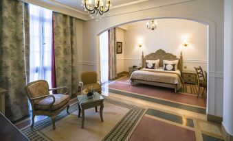 a luxurious bedroom with a large bed , chairs , and a rug on the floor , all surrounded by elegant furniture at Majestic Hotel