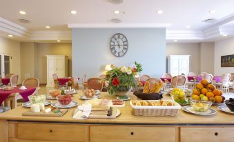 a large dining table is set with a variety of food and drinks , accompanied by a clock on the wall at Hotel Punta Nord Est
