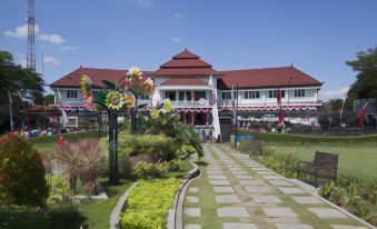 a large white building with a red roof is surrounded by greenery and has a walkway leading up to it at Atria Hotel Malang