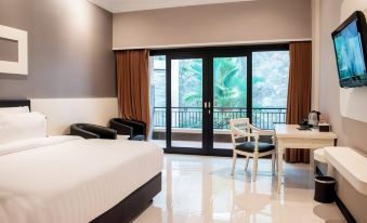 a bedroom with a large bed , white desk , and sliding glass door leading to a balcony at Luminor Hotel Jember by WH