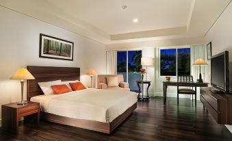 a well - lit bedroom with a large bed , wooden flooring , and a view of the outdoors through large windows at Delonix Hotel Karawang