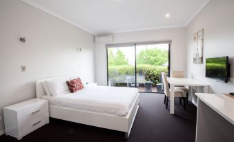 a modern bedroom with a large bed , white bedding , and a view of a garden through the sliding glass door at Springwood Motor Inn