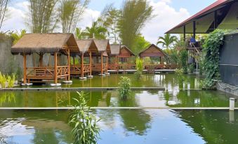 a serene scene of a river with wooden cabins and palm trees , creating a picturesque atmosphere at Borobudur Bed & Breakfast