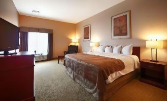 a large bed with a brown blanket and white pillows is in a room with carpeted floors at Best Western High Road Inn